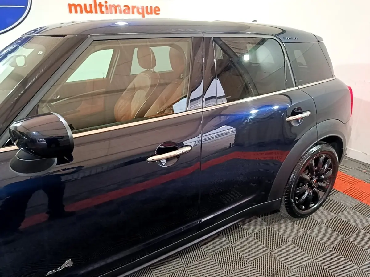 Vue latérale droite d'une MINI Countryman Cooper SE bleu foncé avec jantes noires et intérieur cuir marron visible.