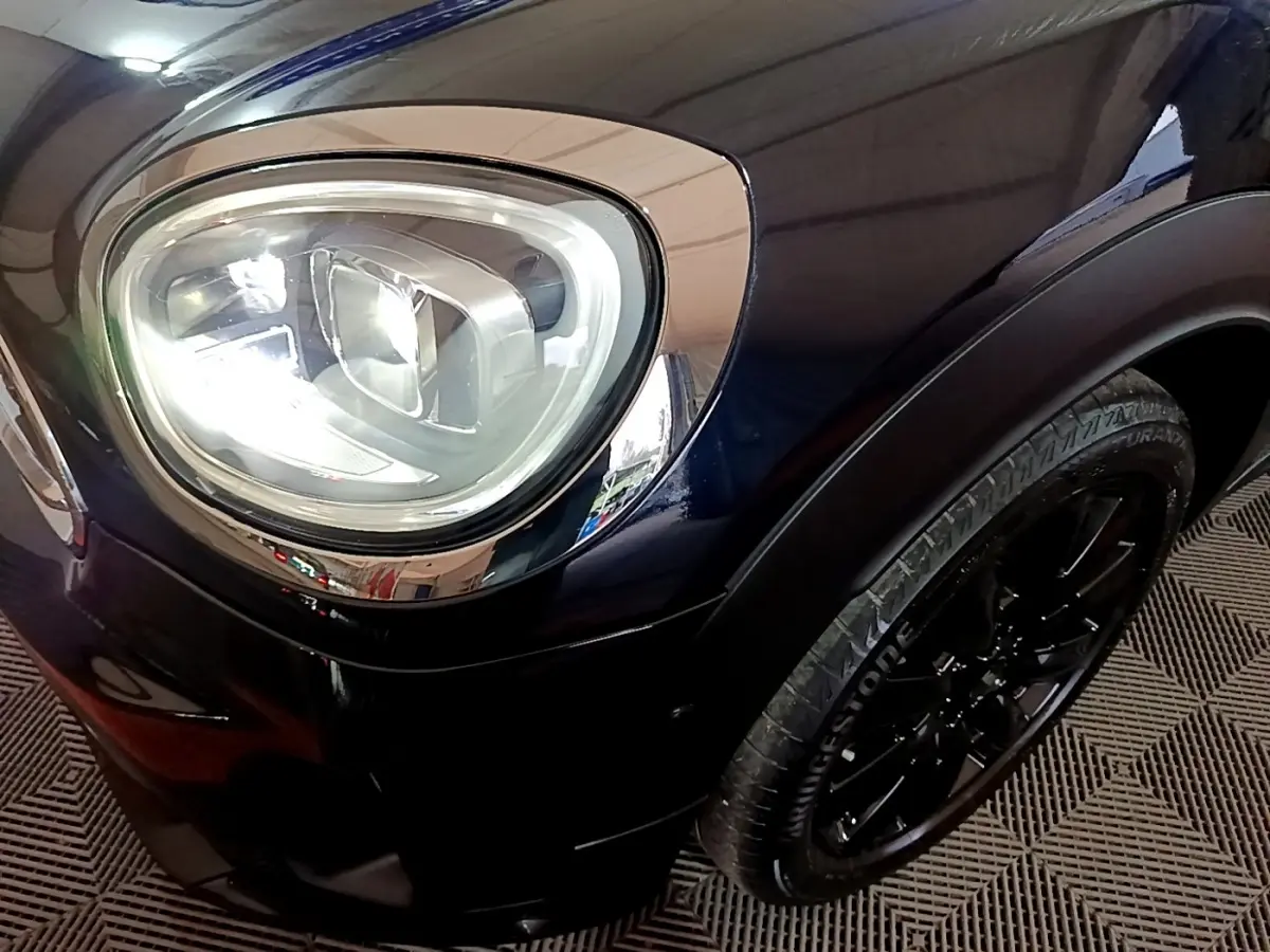 Gros plan sur le phare avant gauche et la roue noire d'une MINI Countryman Cooper SE bleu foncé.