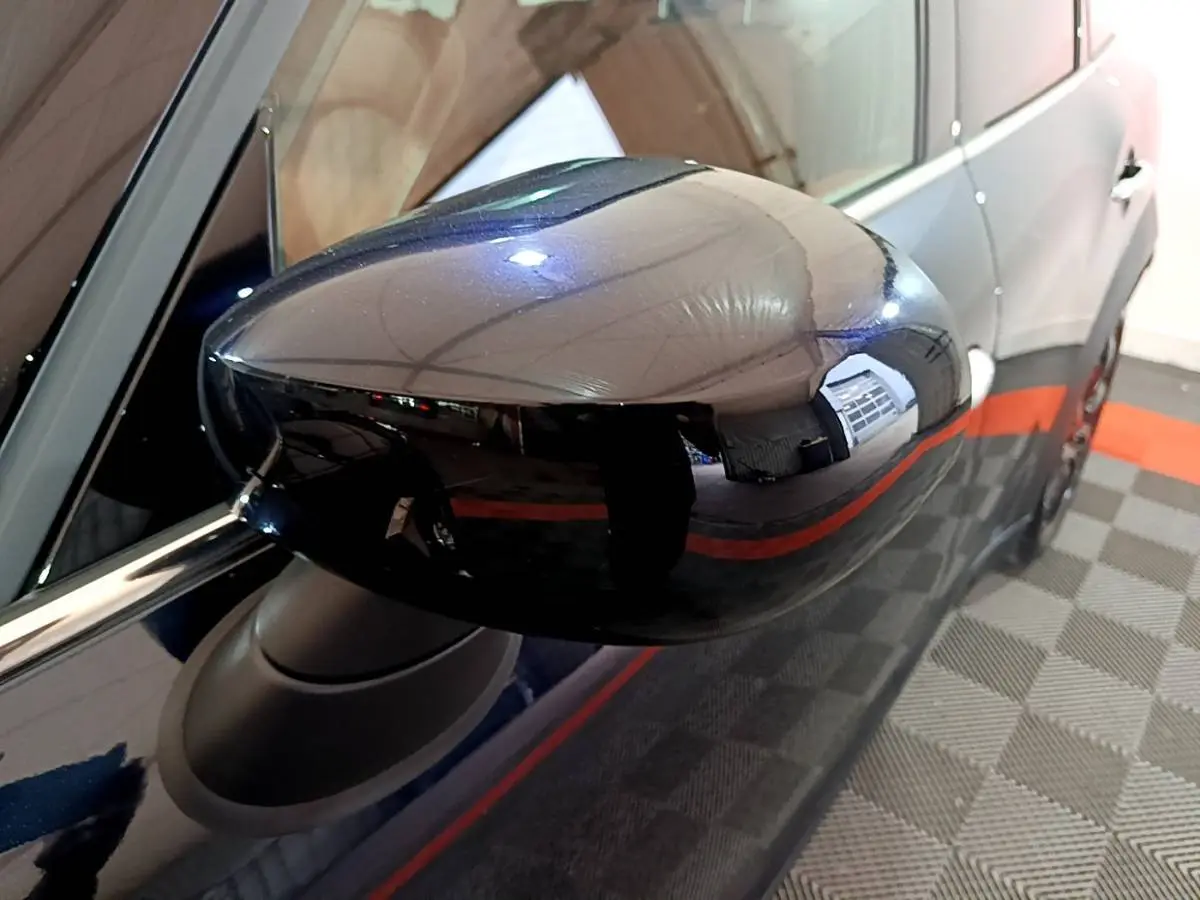 Rétroviseur côté gauche noir brillant d'une MINI Countryman hybride bleu, vue rapprochée sur fond intérieur showroom.