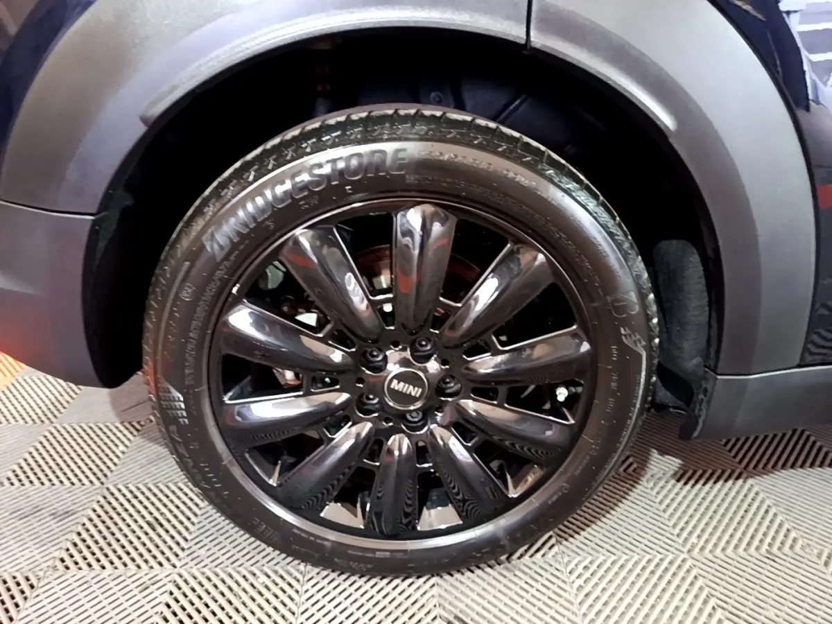 Gros plan sur la roue avant droite noire brillante du MINI Countryman Cooper SE hybride bleu, avec logo MINI central.