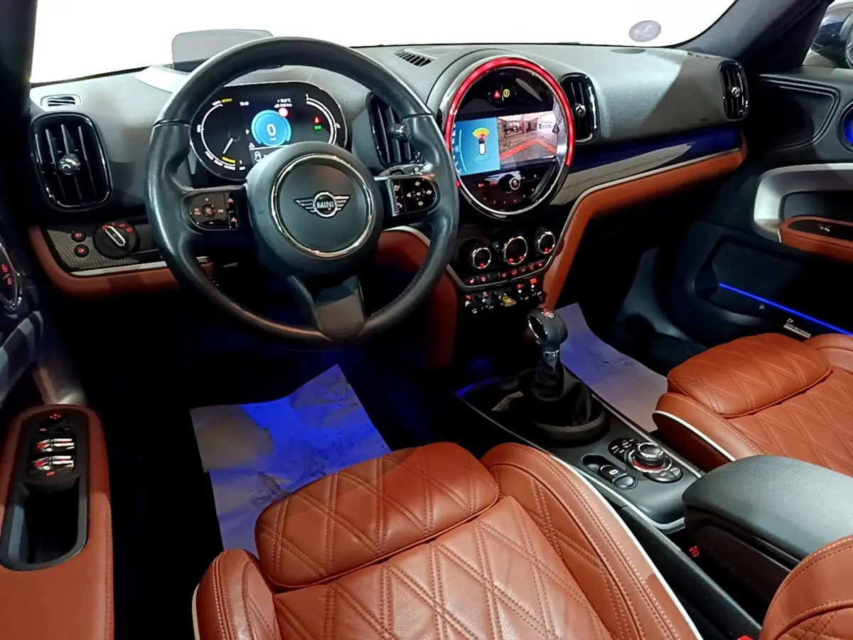 Vue intérieure avant du MINI Countryman Cooper SE avec sièges cuir marron et tableau de bord numérique éclairé.