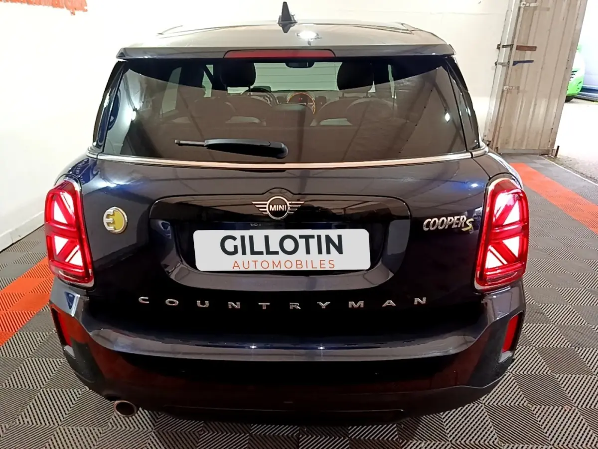 Vue arrière d'une MINI Countryman Cooper SE bleu avec feux arrière LED et logo électrique jaune sur le côté gauche.