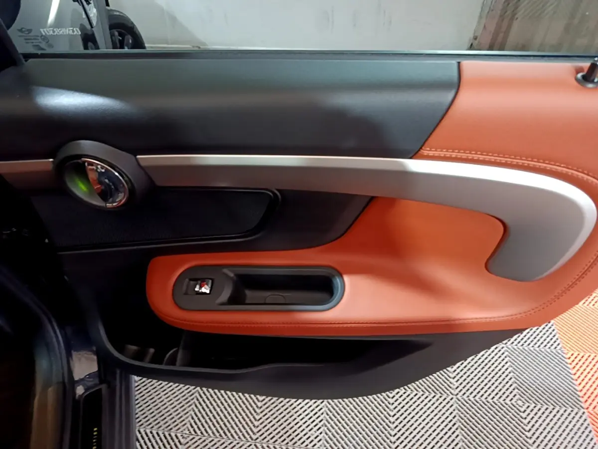 Gros plan sur la porte intérieure côté gauche du MINI Countryman bleu, avec garniture cuir marron et poignée argentée.
