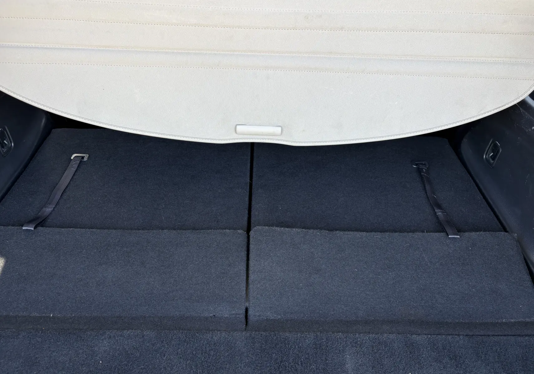 Coffre du Nissan X-TRAIL 2016 White Edition 7 places vu de l'arrière, sièges rabattus et cache-bagages beige partiellement visible.