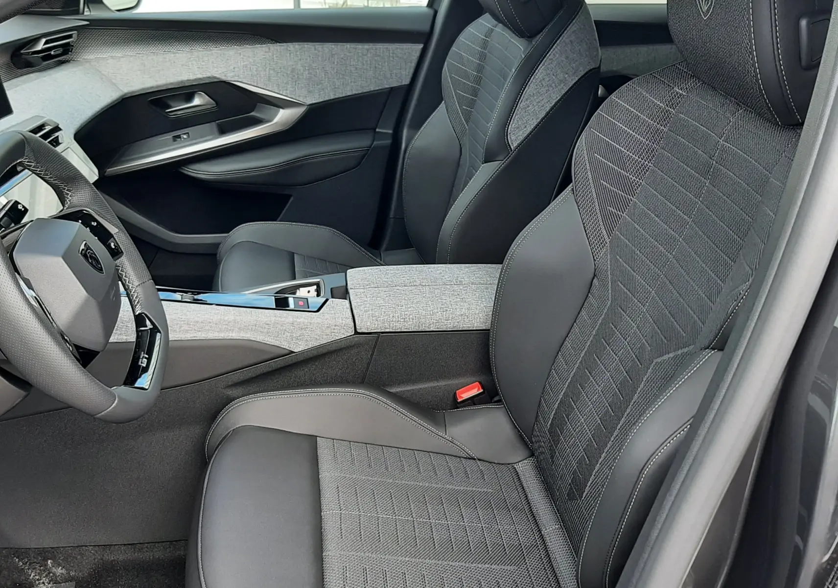 Vue intérieure côté conducteur du Peugeot 3008 gris titane 2026, sièges en tissu et cuir avec logo Peugeot brodé.