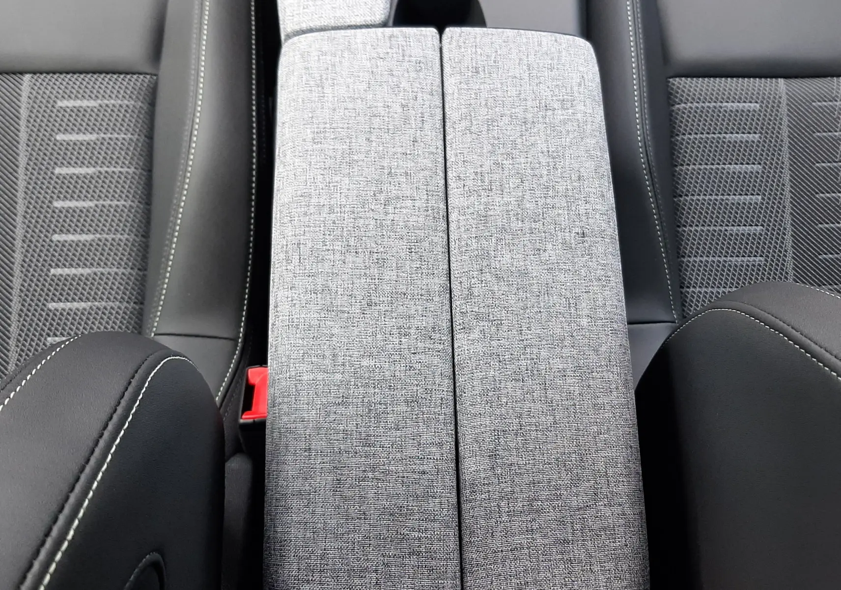 Vue plongeante sur l'accoudoir central gris clair et les sièges noirs en tissu et cuir du Peugeot 3008 Hybrid 2026.