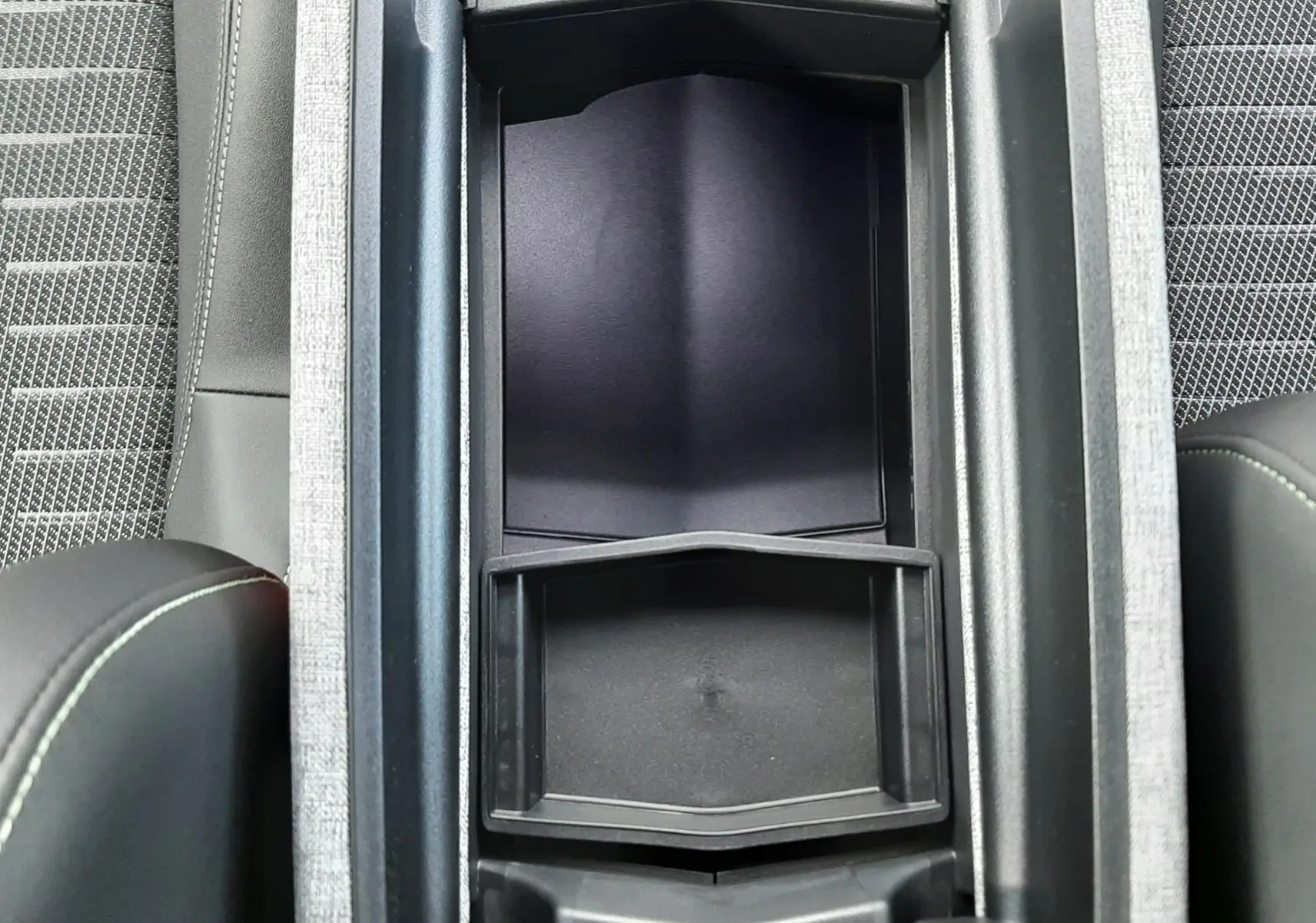 Vue plongeante sur la console centrale ouverte du Peugeot 3008 gris titane, montrant le rangement intérieur et les sièges tissu noir.