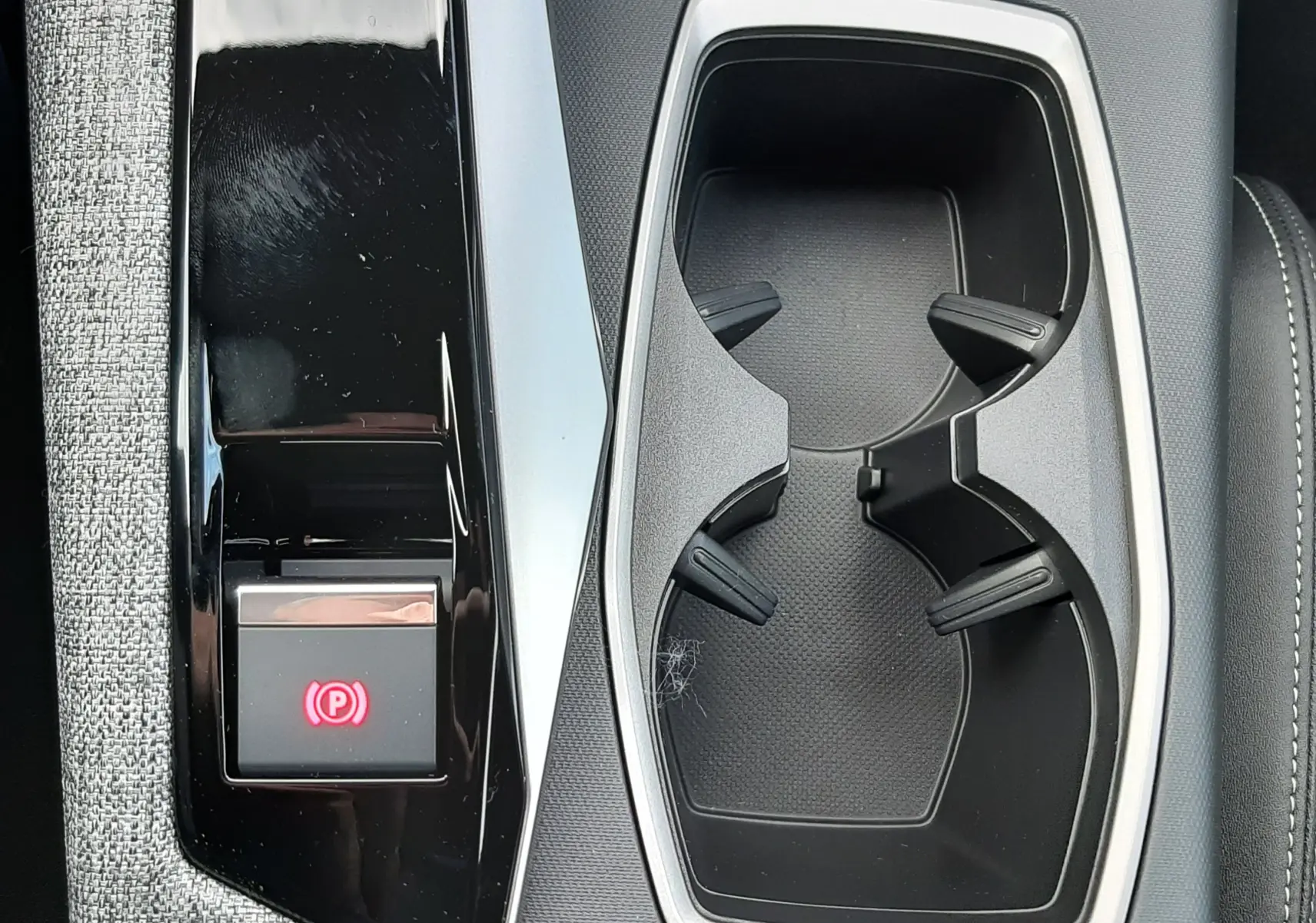 Gros plan sur la console centrale noire et grise du Peugeot 3008 hybride, avec porte-gobelets et bouton frein à main électronique.
