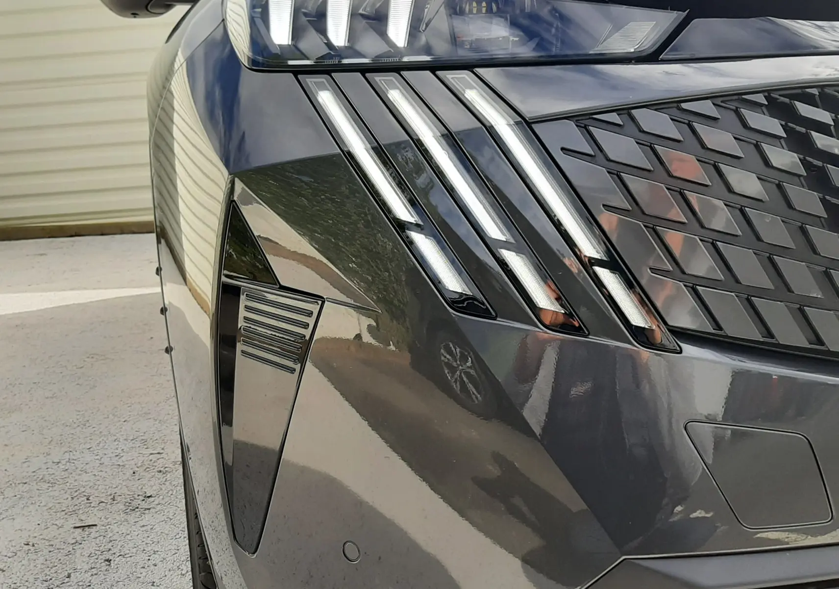 Gros plan sur l'avant droit du Peugeot 3008 gris titane, mettant en valeur ses phares LED et la calandre distinctive.