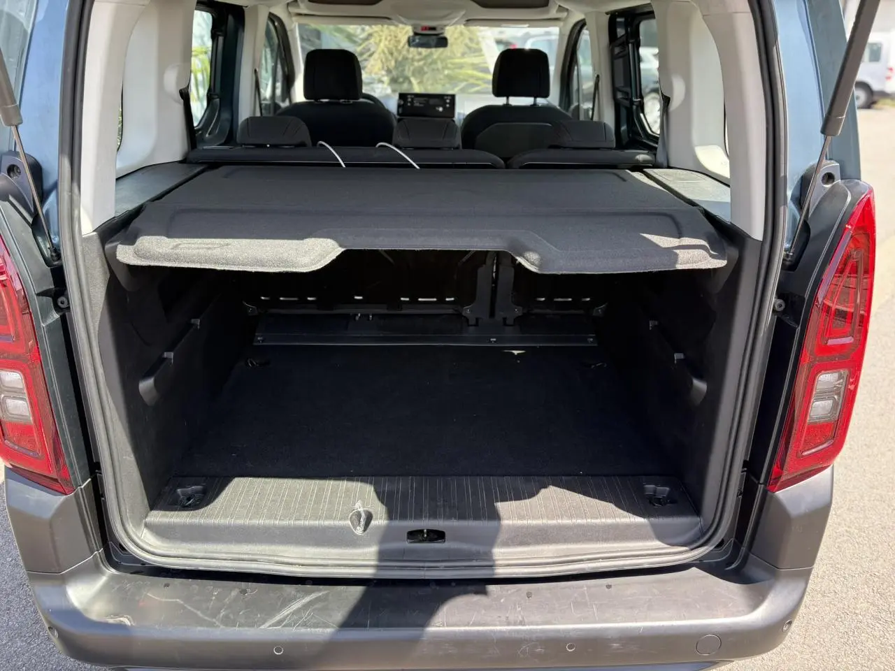 Coffre ouvert vu de l'arrière d'un Citroën Berlingo ë-136 bleu Kiama avec cache-bagages et sièges arrière rabattus.