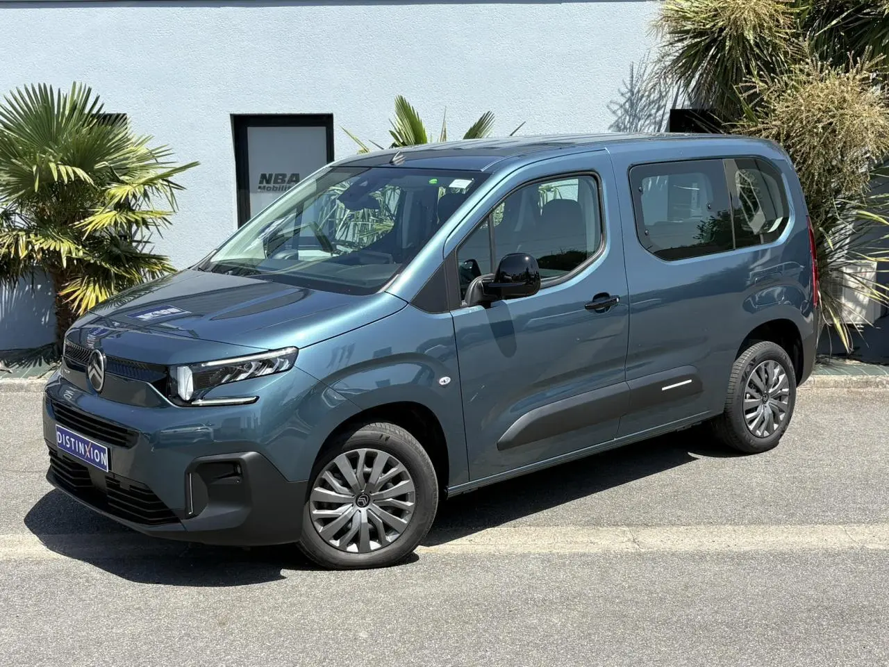 Vue 3/4 avant droit du Citroën Berlingo ë-136 54kWh bleu Kiama avec jantes tôles et porte coulissante droite visible.