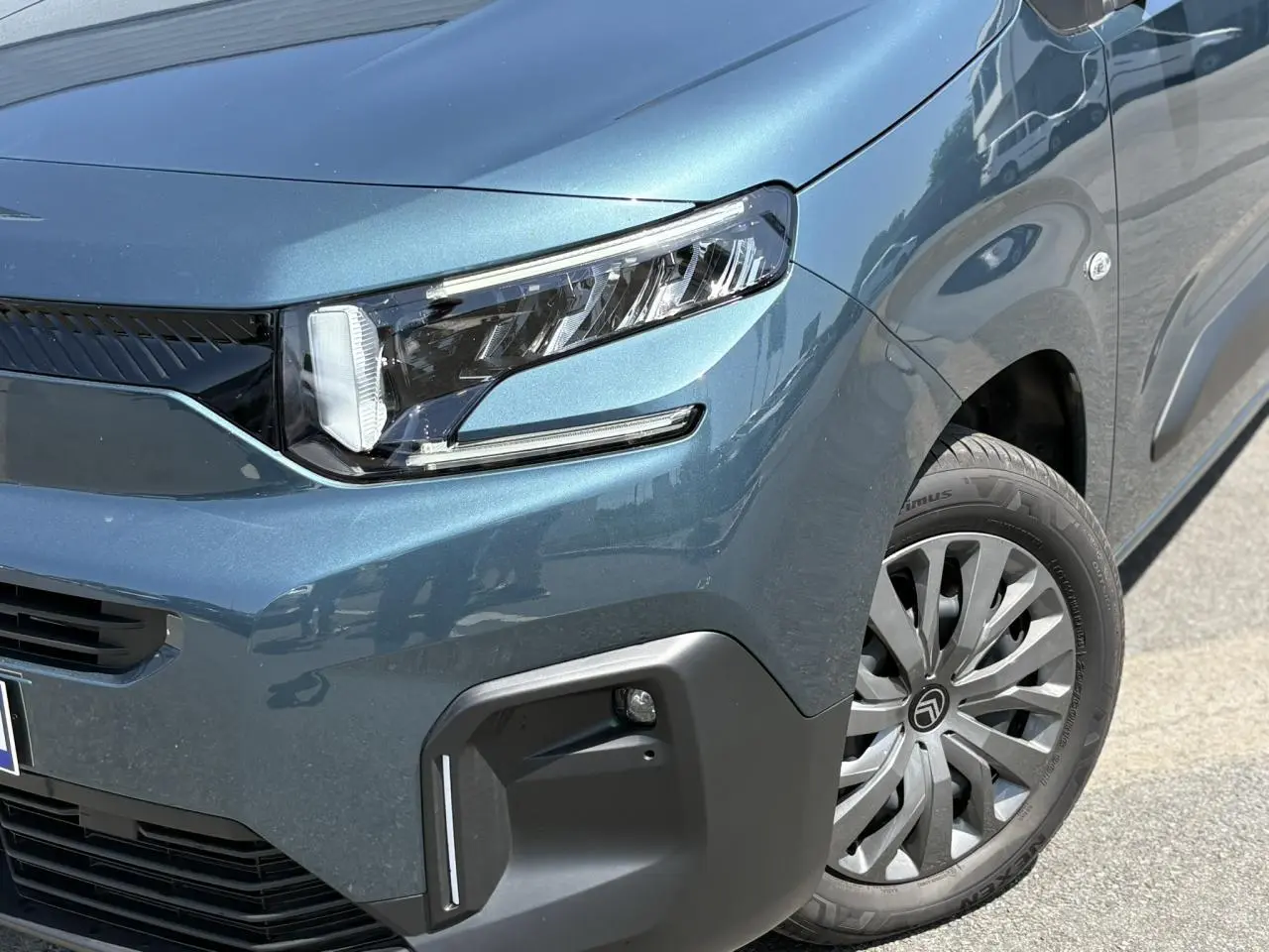 Gros plan sur l’avant droit du Citroën Berlingo ë-136 bleu Kiama, mettant en valeur le phare LED et la jante tôlée avec enjoliveur.