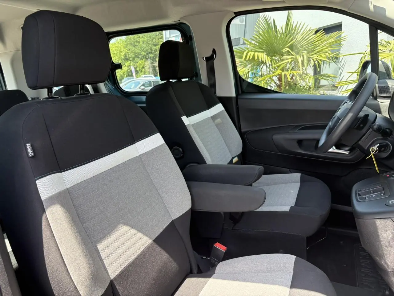 Vue intérieure côté conducteur du Citroën Berlingo ë-136 2025, sièges tissu Urban Grey avec accoudoirs.