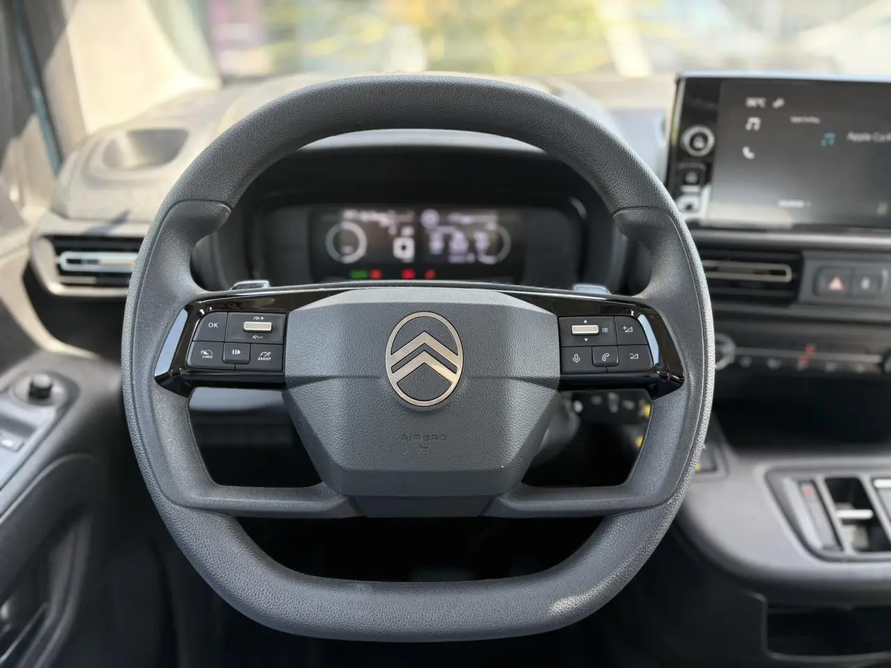 Vue frontale du volant multifonction noir du Citroën Berlingo ë-136 avec tableau de bord numérique et écran tactile.