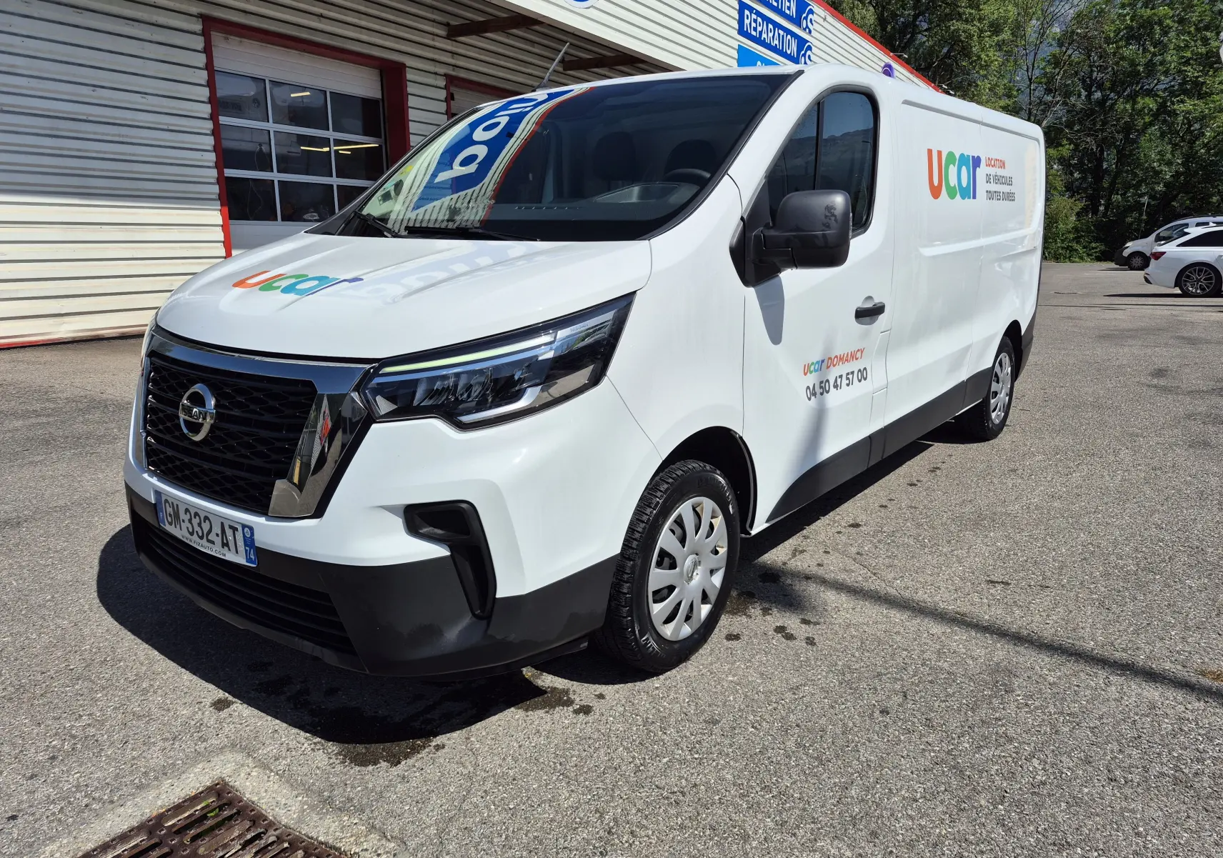 Nissan Primastar blanc en 3/4 avant droit, utilitaire avec logo coloré Ucar sur la porte latérale.