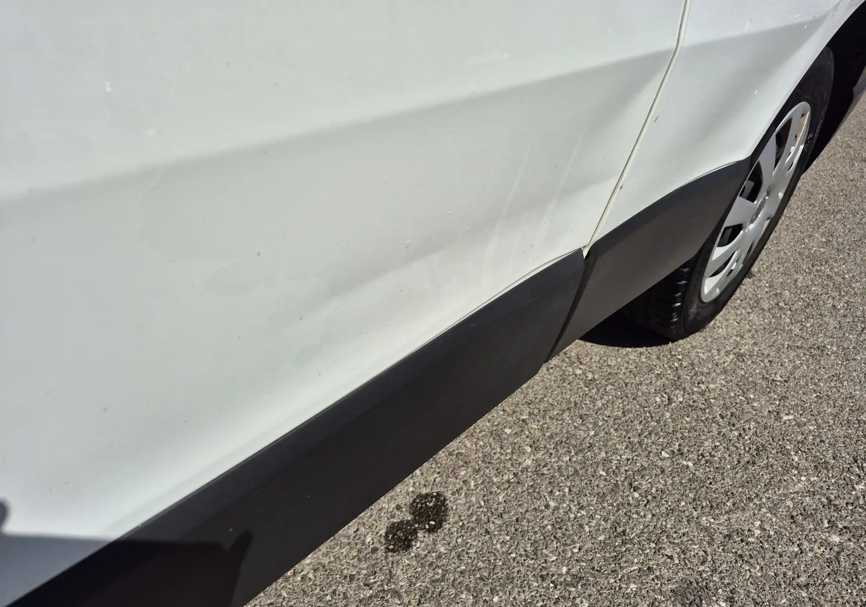 Détail du côté droit arrière blanc du Nissan Primastar avec une rayure visible sur la porte et une roue partielle.