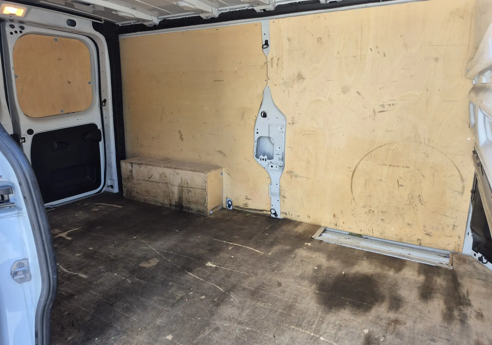 Vue intérieure arrière du fourgon blanc Nissan Primastar, montrant l'espace de chargement avec parois en bois et sol marqué.