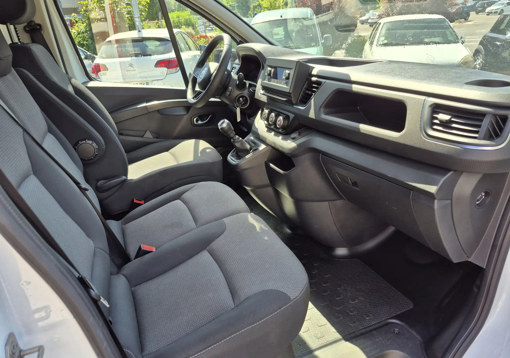 Vue intérieure côté conducteur du Nissan Primastar blanc, montrant les sièges avant, le volant multifonction et la console centrale avec boîte manuelle.
