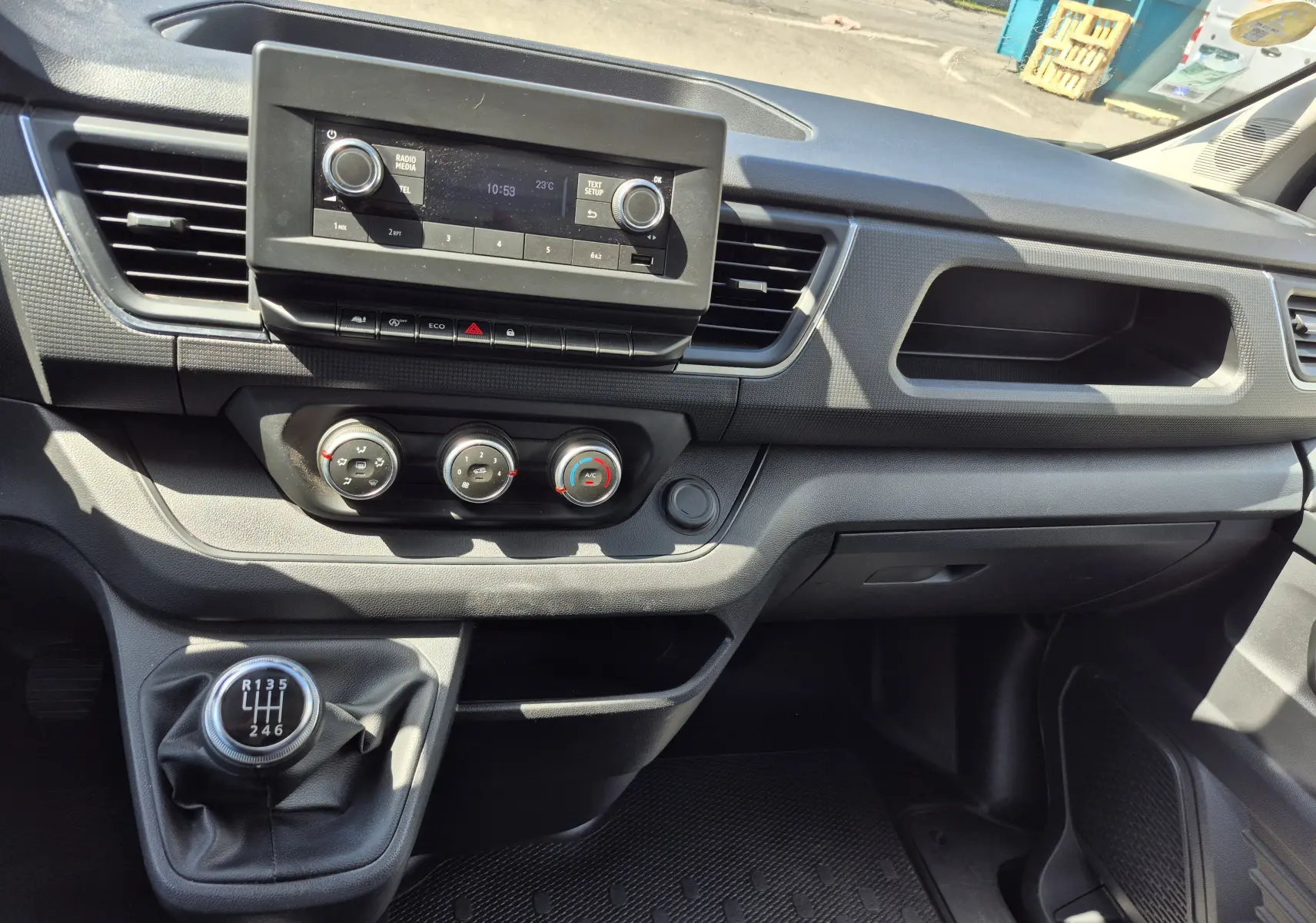 Vue intérieure du tableau de bord du Nissan Primastar blanc, avec console centrale et levier de vitesses manuel en évidence.