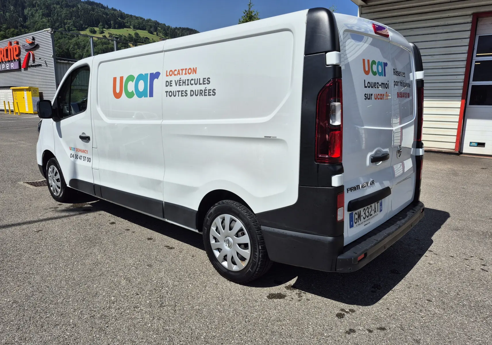 Vue 3/4 arrière droite d’un utilitaire Nissan Primastar blanc avec marquage publicitaire Ucar sur la carrosserie.