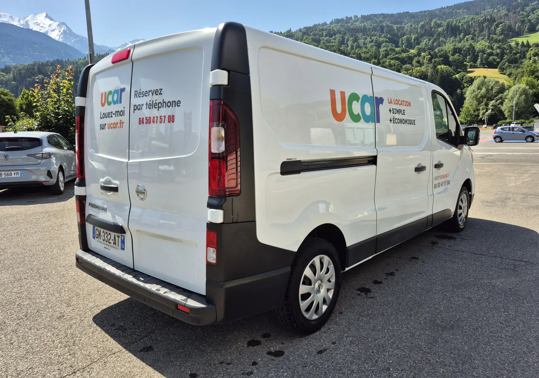Vue 3/4 arrière droite d’un utilitaire Nissan Primastar blanc avec marquage publicitaire coloré ucar sur la carrosserie.