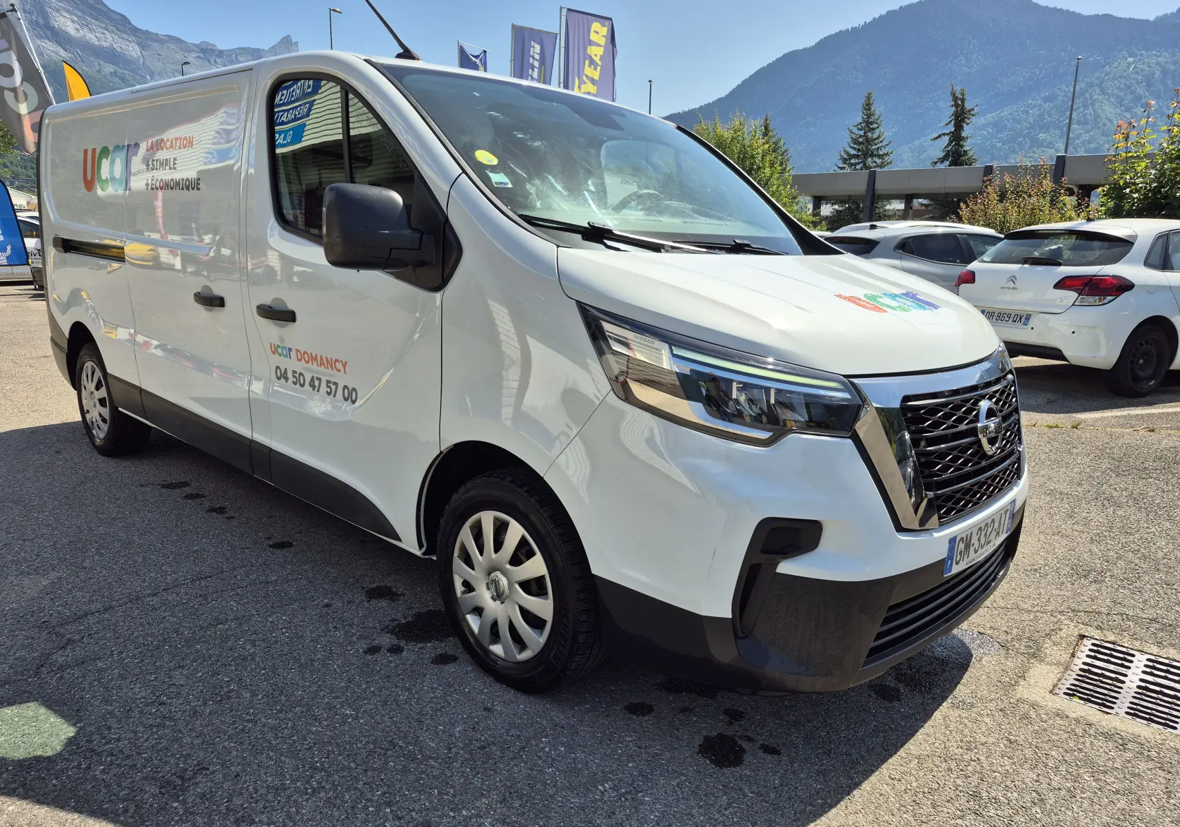 Vue 3/4 avant droit d’un utilitaire Nissan Primastar blanc avec marquage publicitaire Ucar sur porte latérale.
