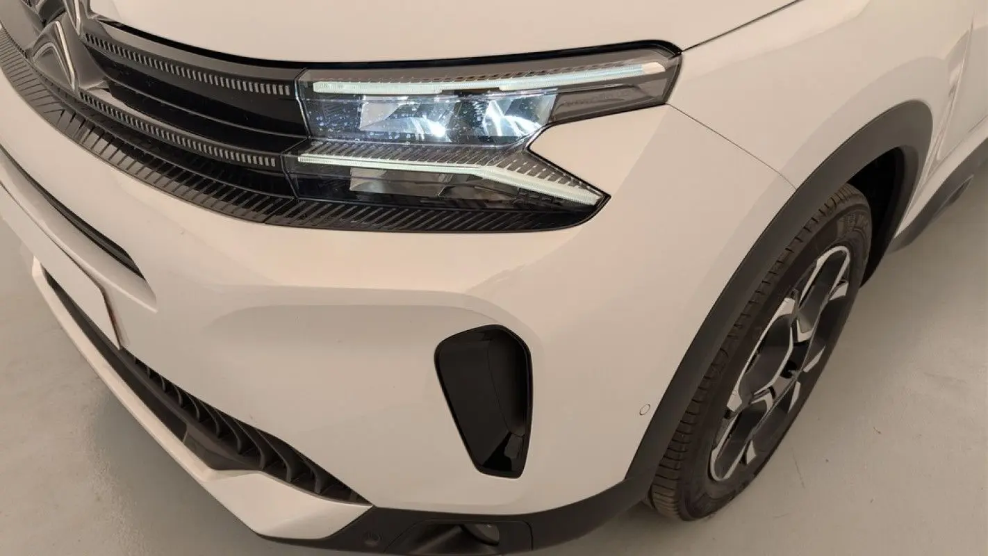Gros plan sur l'avant droit blanc Okenite du Citroën C5 Aircross 2025 avec phares LED et jante alliage distinctive.