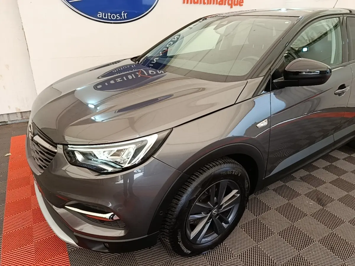 Vue 3/4 avant droit d'un Opel Grandland X gris foncé avec jantes alliage et phares LED visibles en intérieur showroom.