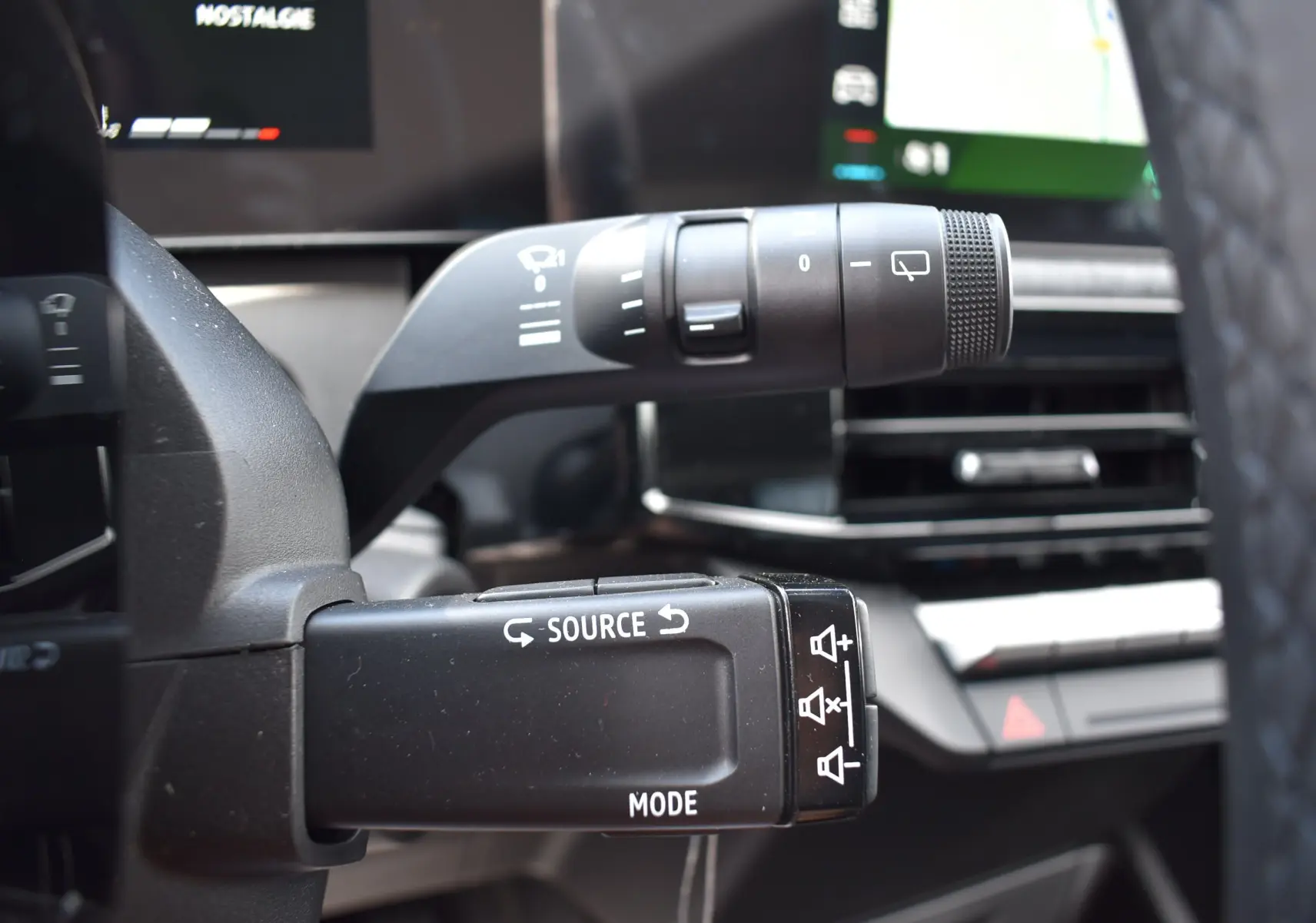 Gros plan sur la commande audio au volant de la Renault Clio VI gris schiste, avec écran tactile en arrière-plan.