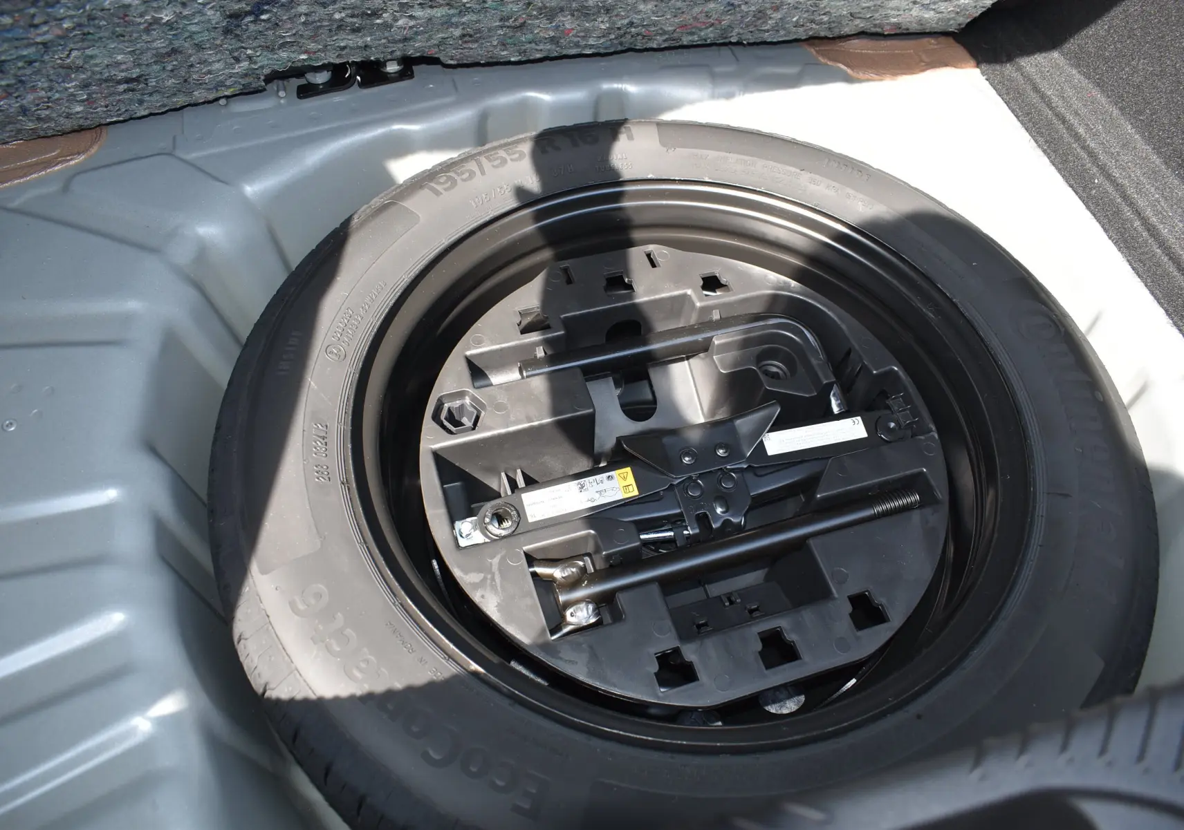 Gros plan sur la roue de secours et son kit de réparation dans le coffre d’une Renault Clio VI gris schiste.