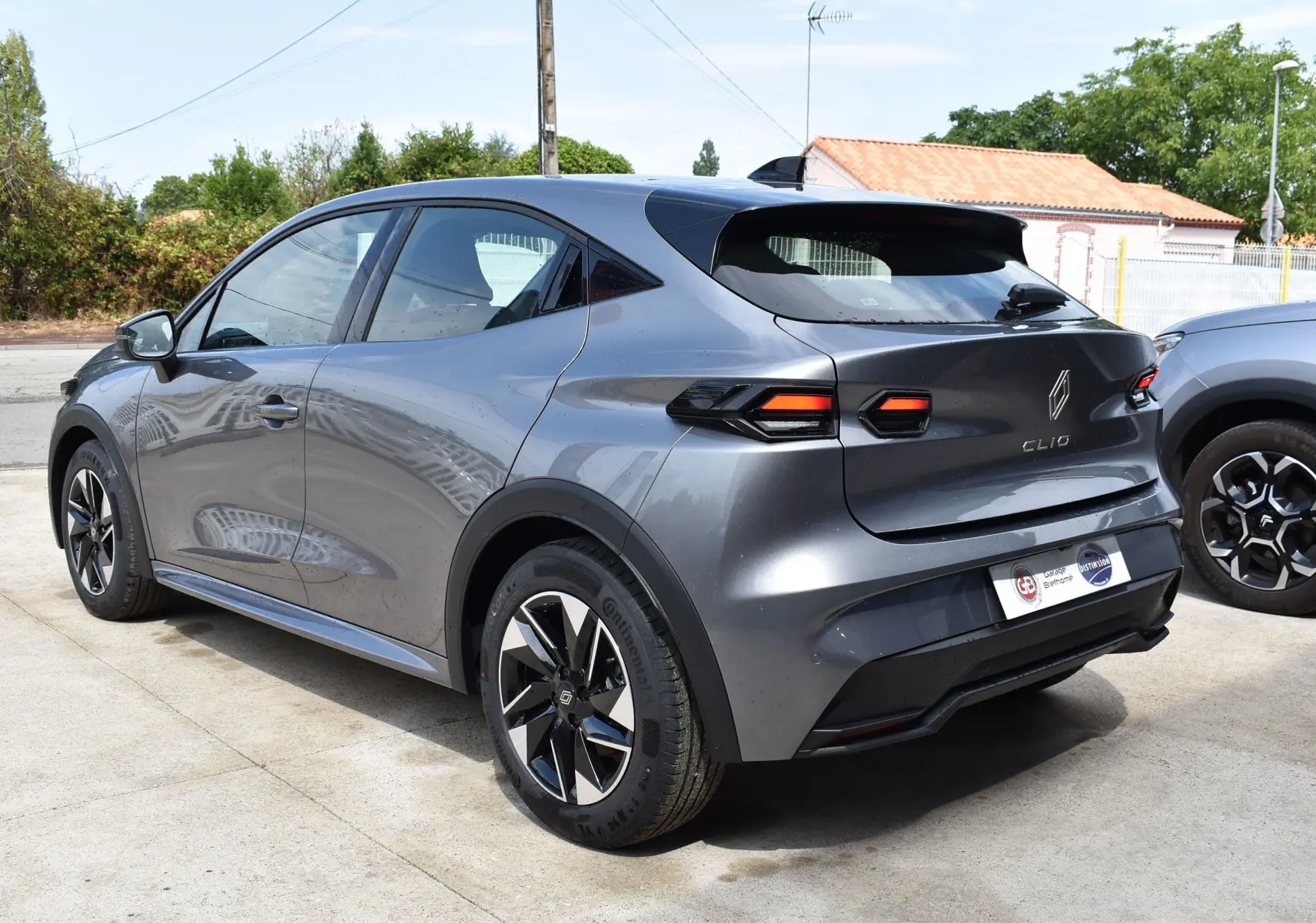 Vue 3/4 arrière droite d'une Renault Clio VI gris schiste avec jantes noires et spoiler de toit noir.