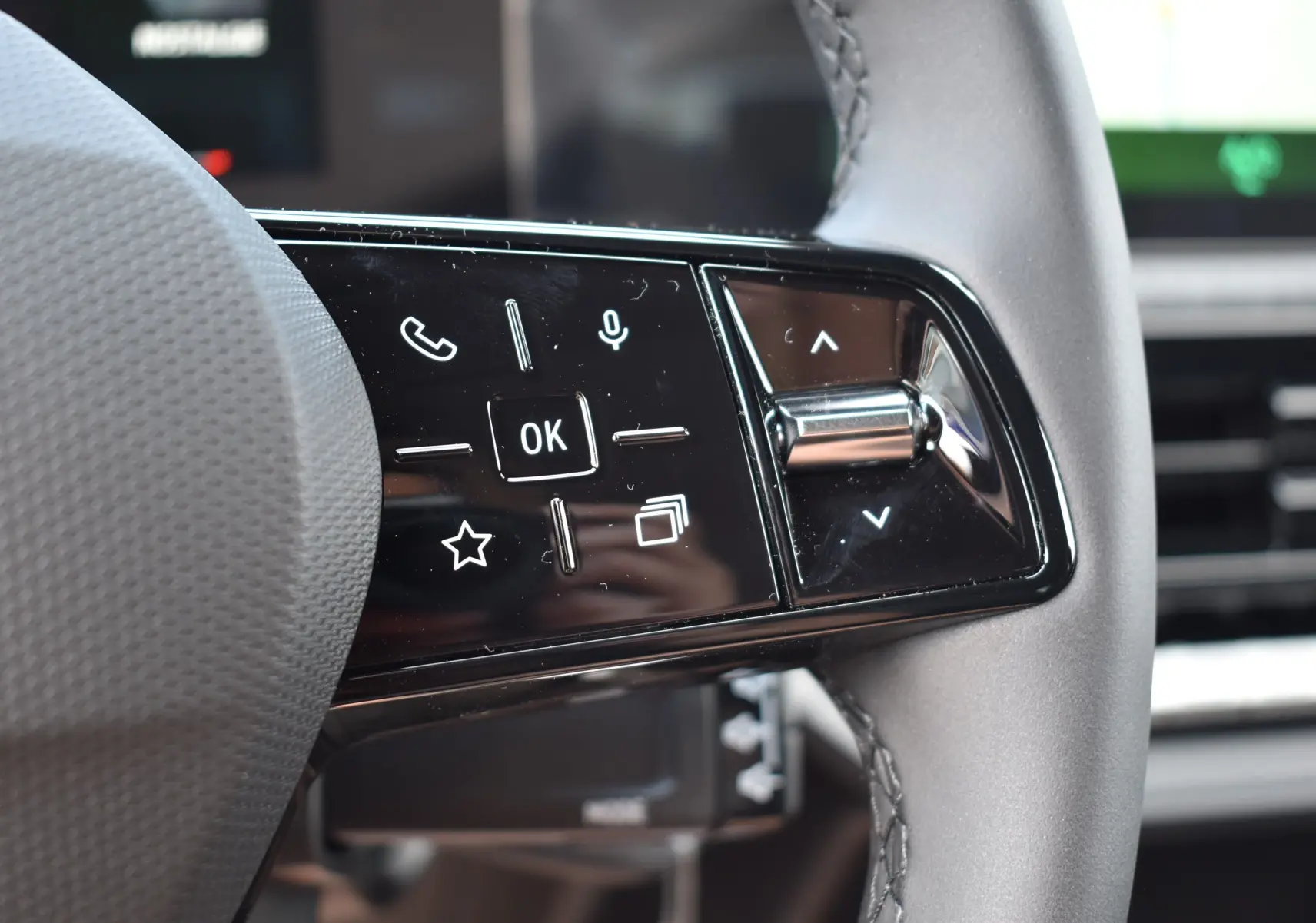 Gros plan sur les commandes multifonctions noires du volant de la Renault Clio VI gris schiste, avec touches tactiles et molette.