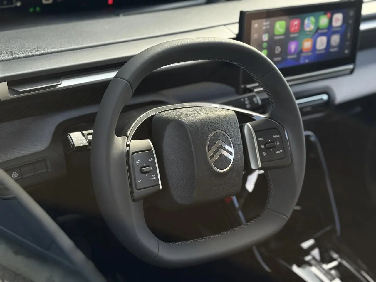 Gros plan sur le volant multifonctions carré noir du Citroën C3 Aircross 2025 avec écran tactile en arrière-plan.