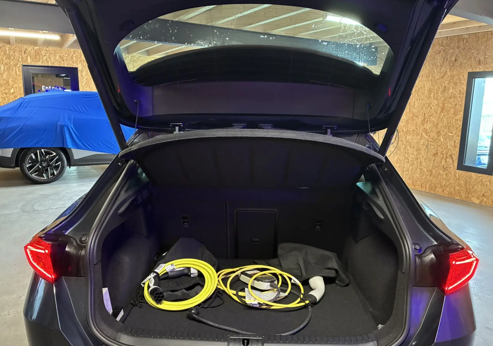 Coffre ouvert vu de l’arrière d’un CUPRA Formentor gris 2023, avec câbles de recharge hybride visibles.