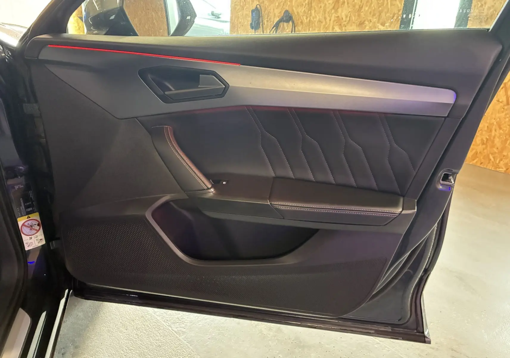 Vue intérieure du panneau de porte avant gauche gris foncé du CUPRA Formentor 1.4 e-Hybrid 2023 avec surpiqûres et éclairage d'ambiance rouge.