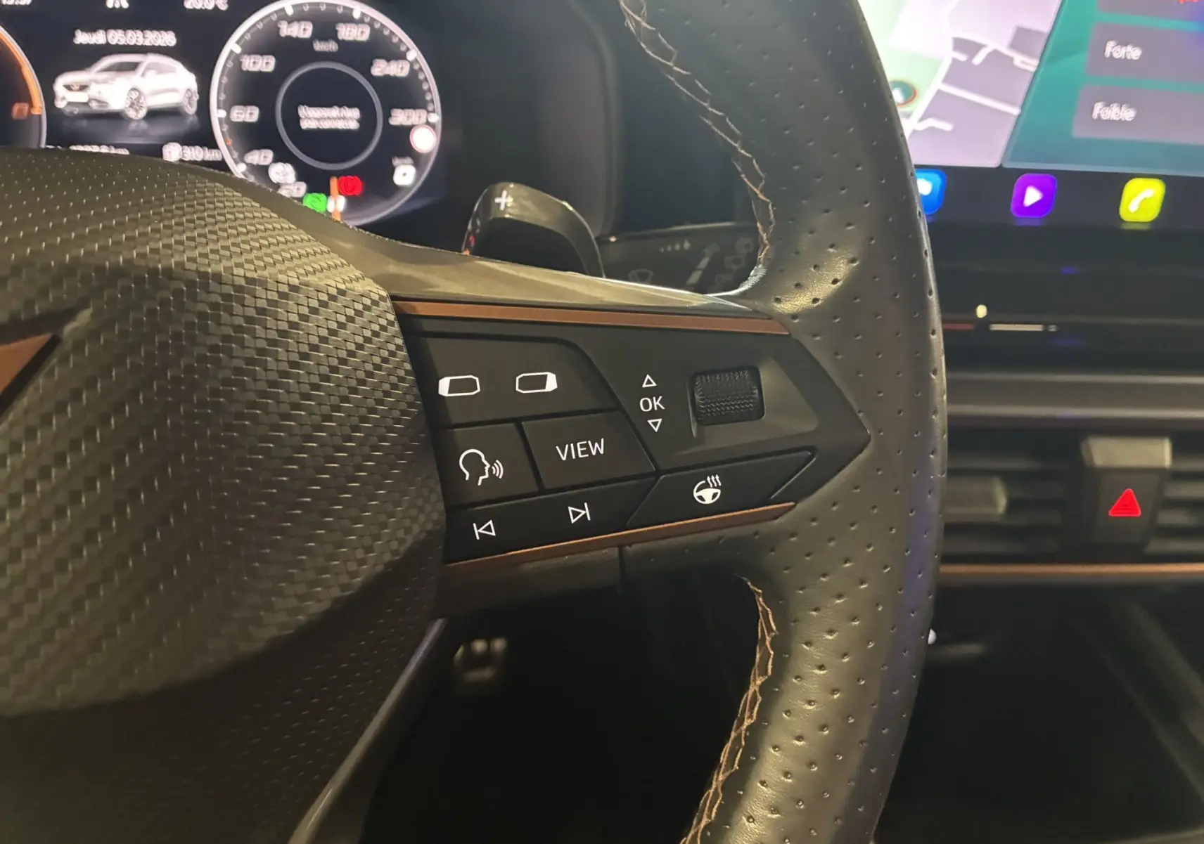 Gros plan sur le volant cuir perforé du CUPRA Formentor 1.4 e-Hybrid avec commandes multifonctions et écran numérique en arrière-plan.