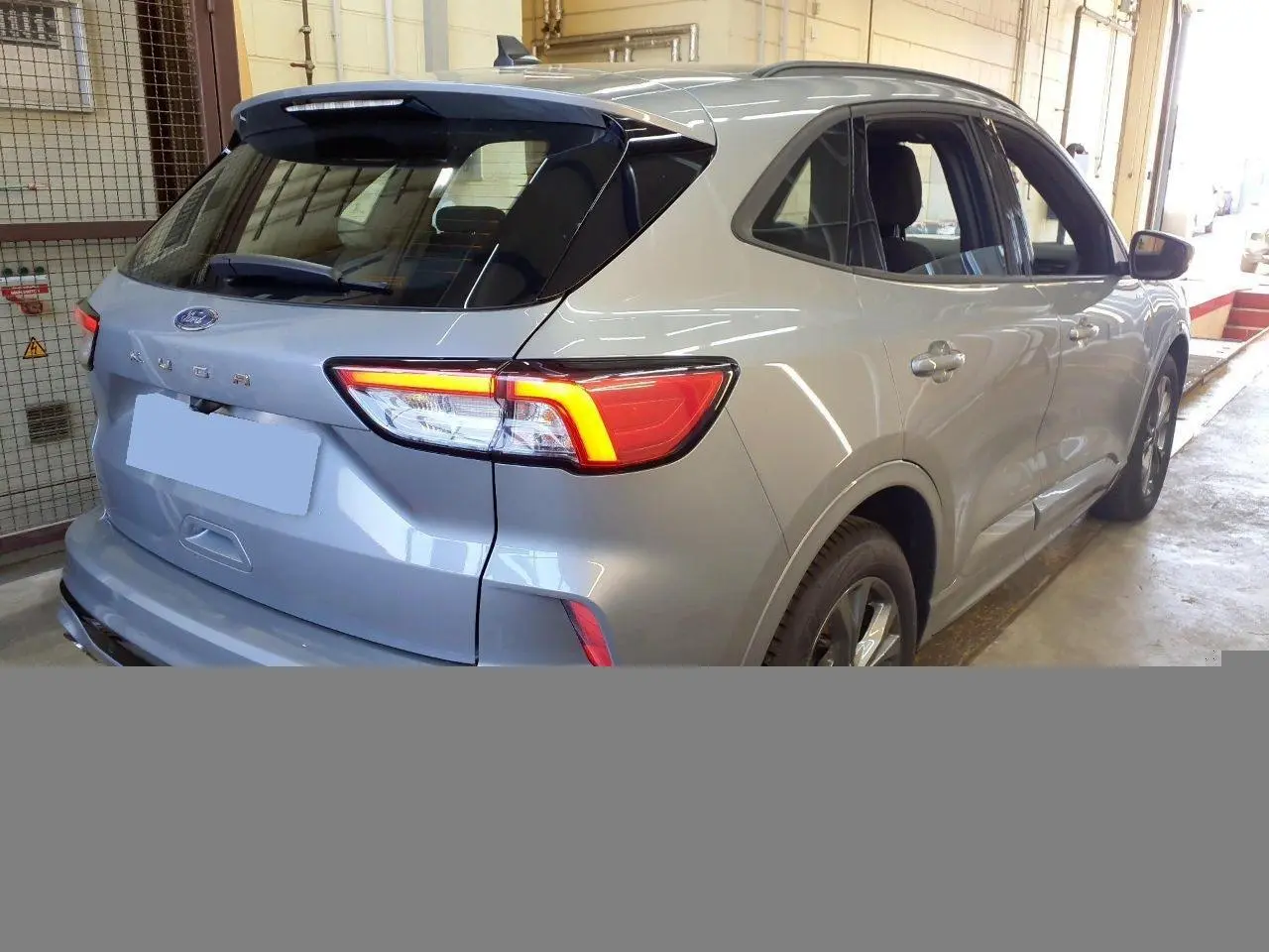 Vue 3/4 arrière droite du Ford Kuga 2.0 EcoBlue gris Solar avec feux arrière allumés en intérieur.