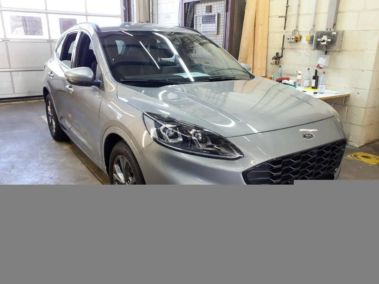 Vue 3/4 avant gauche du Ford Kuga 2024 gris Solar avec calandre noire et phares LED dans un garage.