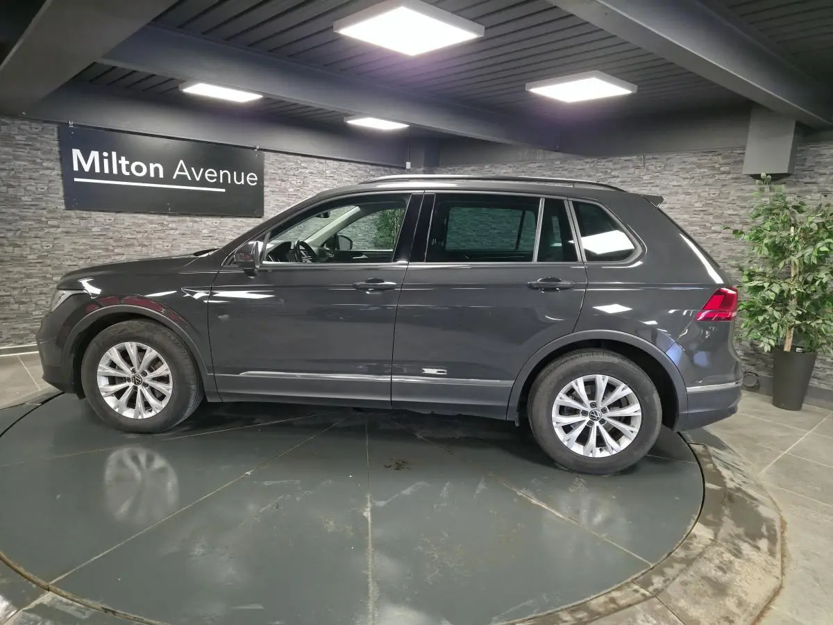 Vue de profil côté gauche d’un Volkswagen Tiguan gris métallisé 2022 dans un showroom intérieur.