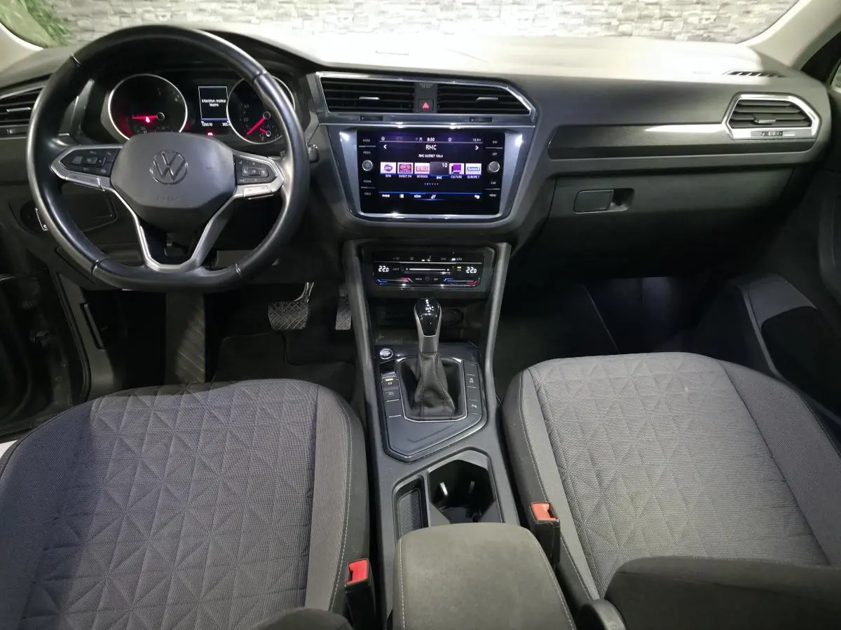 Vue intérieure frontale du tableau de bord et console centrale du Volkswagen Tiguan gris avec sellerie tissu et volant multifonctions cuir.