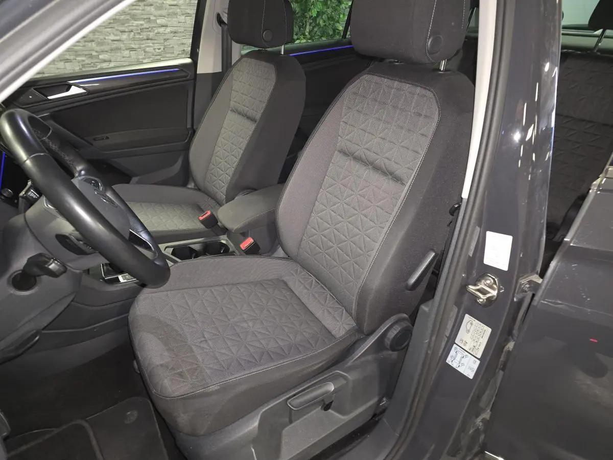 Vue intérieure côté conducteur du Volkswagen Tiguan gris 2022, sièges tissu avec motifs géométriques et éclairage d'ambiance bleu.
