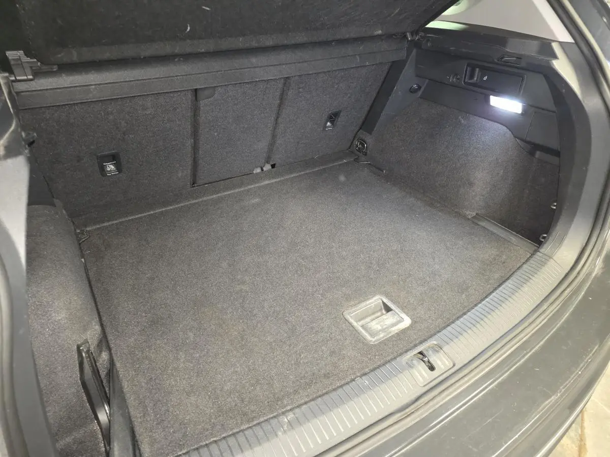 Coffre ouvert du Volkswagen Tiguan gris, vue plongeante montrant le plancher et l’éclairage intérieur à droite.