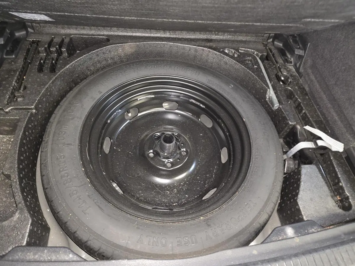 Gros plan sur la roue de secours compacte noire dans le coffre du Volkswagen Tiguan gris, version 2022.