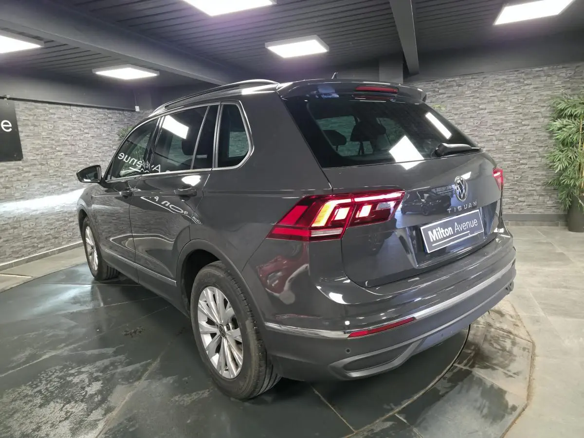 Volkswagen Tiguan gris 3/4 arrière droit en intérieur, feux arrière LED allumés et jantes alliage 17 pouces.