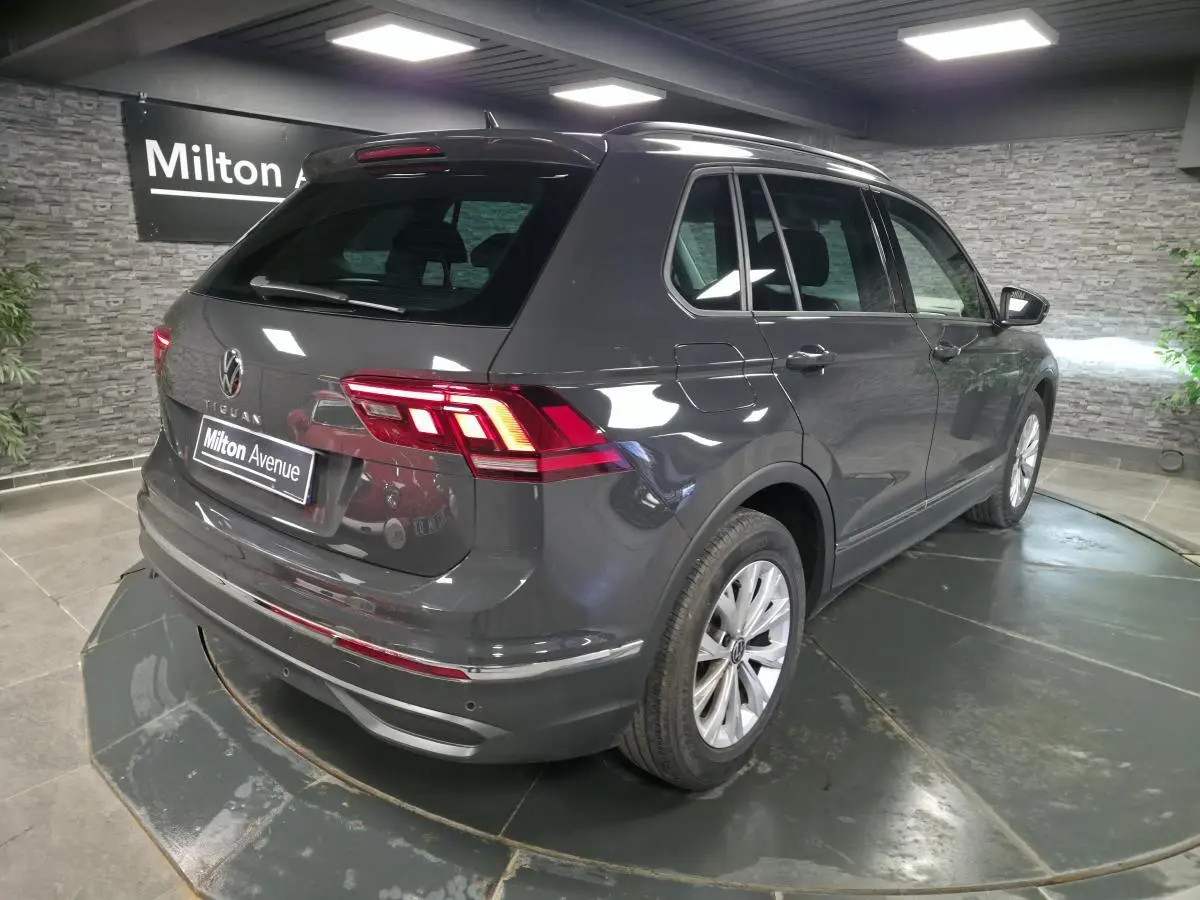 Volkswagen Tiguan gris en 3/4 arrière droit, avec feux LED et jantes alliage 17 pouces visibles en intérieur showroom.