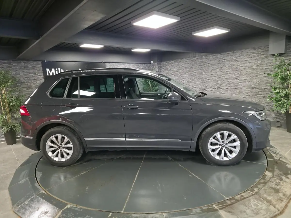 Vue latérale droite d'un Volkswagen Tiguan gris métallisé 2022 dans un showroom intérieur avec éclairage LED.