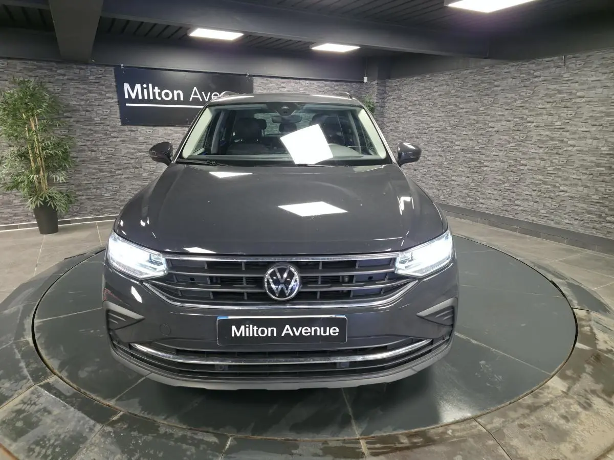 Vue avant d'un Volkswagen Tiguan gris métallisé avec feux LED allumés dans un showroom intérieur.