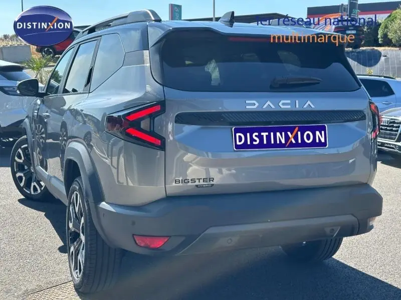 Vue 3/4 arrière droite du Dacia Bigster gris schiste avec feux arrière LED en forme de flèche et barres de toit visibles.