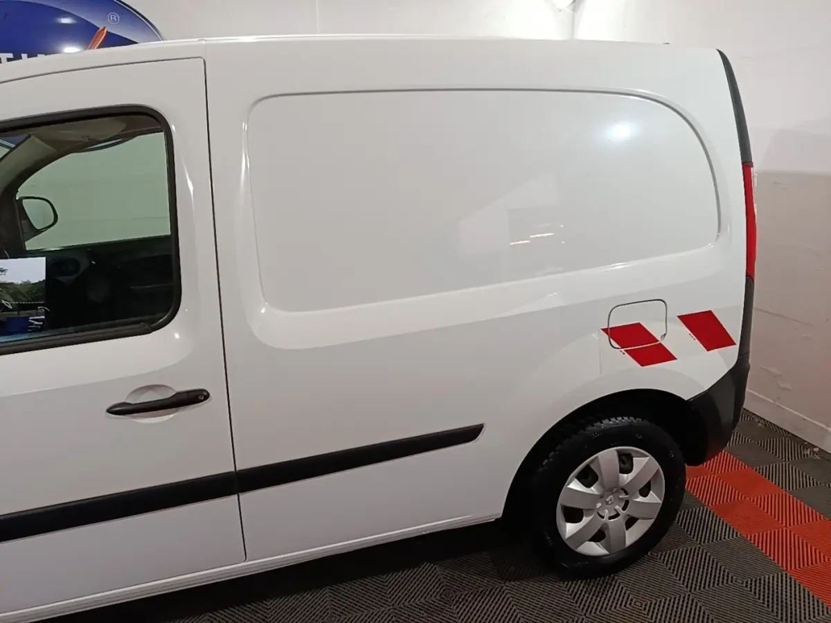 Vue latérale droite d’un Renault Kangoo blanc avec marquages rouges sur l’aile arrière et jantes argentées.