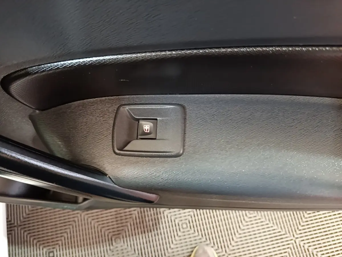Gros plan sur le bouton de commande de la vitre électrique sur la porte intérieure noire d’un Renault Kangoo blanc.